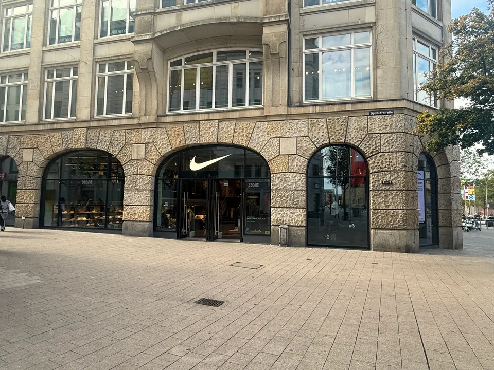 Nike-Geschäft in Rundbogenarkaden eines Natursteingebäudes an der Spitalerstraße, davor eine leere gepflasterte Fußgängerzone