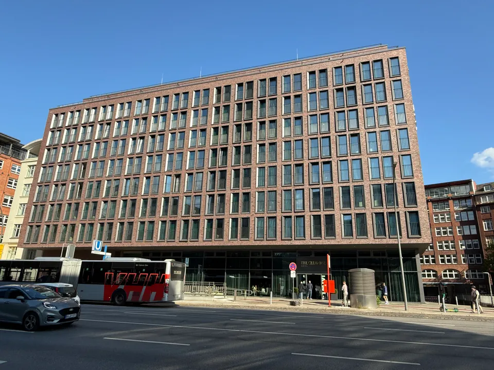 Neungeschossiges Hotel aus rotbraunem Klinker an einer mehrspurigen Straße, davor ein Bus und ein Auto