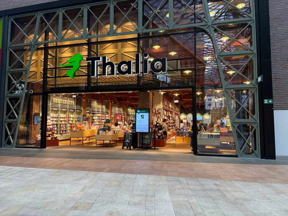 Eingang einer Thalia-Buchhandlung mit grünem Stahlfachwerk, leuchtendem Schriftzug und beleuchteten Bücherregalen im Inneren