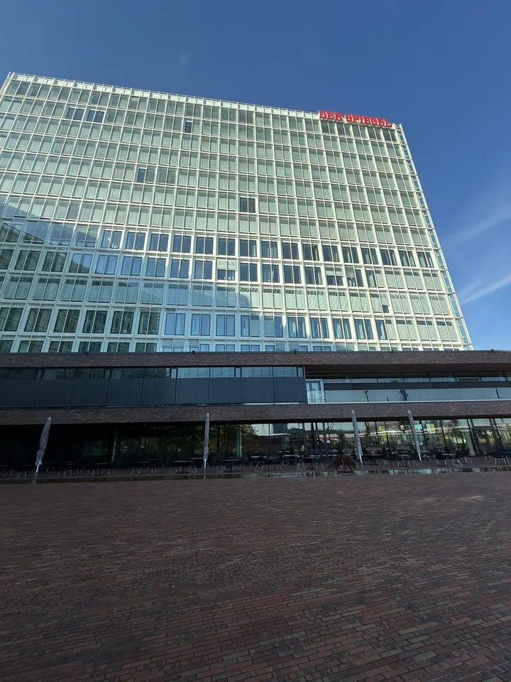 Glasfassade des SPIEGEL-Gebäudes mit Außengastronomie im Erdgeschoss hinter einem leeren Klinkerplatz