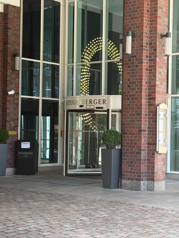 Drehtür mit Schriftzug Steigenberger, dahinter leuchtende Lichtinstallation in Bogenform, davor Buchskugel im Pflanzkübel