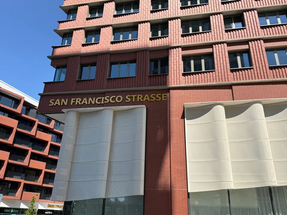 Rote Ziegelfassade mit goldenem Schriftzug San Francisco Strasse über hellen, wellenförmigen Fassadenelementen