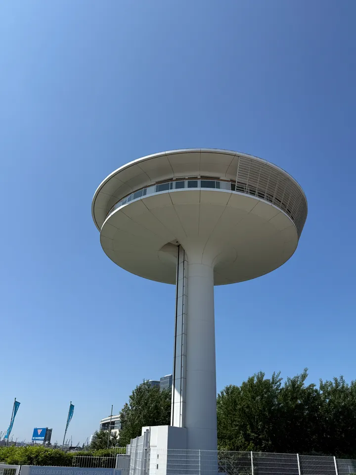 Weißer Turm mit scheibenförmigem Aufbau und Fensterband, von unten gegen wolkenlosen blauen Himmel fotografiert