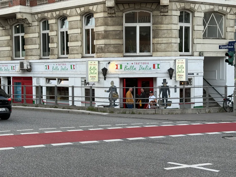 Eckhaus mit Gründerzeitfassade und dem Restaurant Trattoria Bella Italia im Erdgeschoss, davor eine Straße mit rotem Radweg