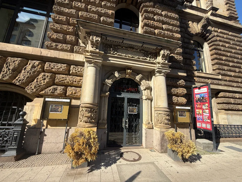 Verziertes Sandsteinportal des Ratsweinkellers mit Glastür, Schaukästen und rotem Aufsteller des Restaurants Parlament