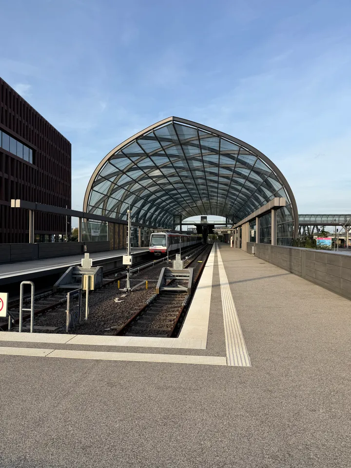 Hochformatige Ansicht der gewölbten Glashalle eines Hochbahnhofs mit U-Bahn-Zug und Gleisenden im Vordergrund