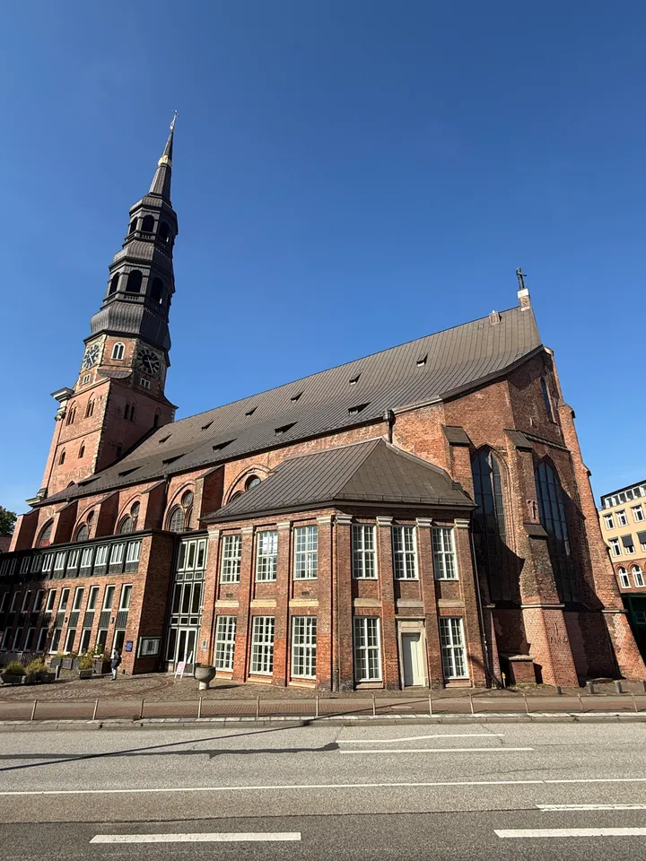 Backsteinkirche mit Turm, gotischen Chorfenstern und Anbau, im Vordergrund eine mehrspurige Straße