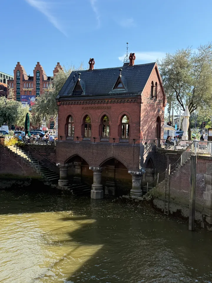 Rotes Backsteinhäuschen auf Säulenbögen über einem Fleet, im Hintergrund ein Speichergebäude mit Museumsaufschrift