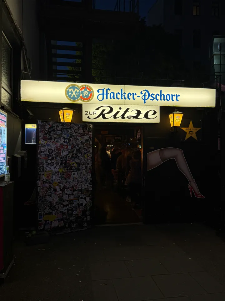 Nächtlicher Eingang der Kneipe Zur Ritze mit Hacker-Pschorr-Leuchtschild, Laternen und aufgemaltem Frauenbein