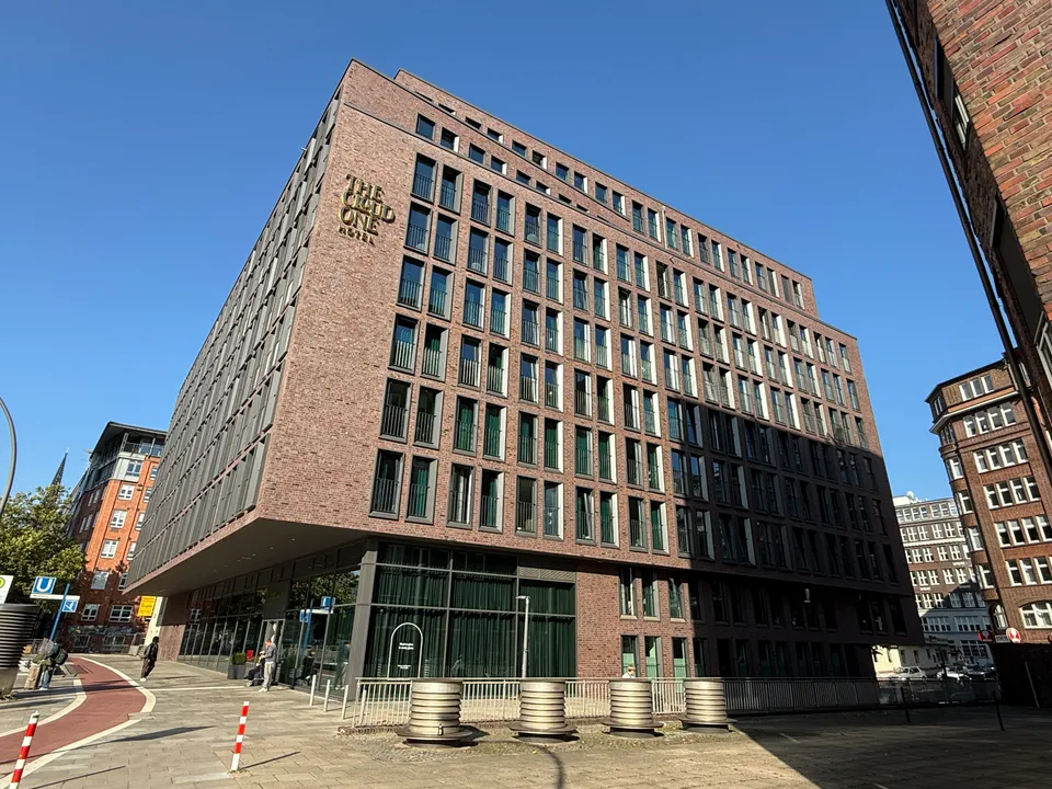Eckansicht eines großen Hotels aus rotem Klinker mit goldenem Schriftzug an der Fassade, blauer Himmel
