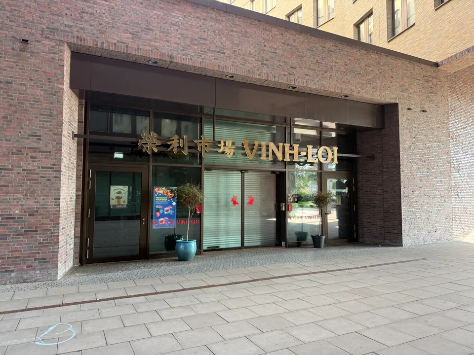 Eingang eines Asia-Markts mit goldener Aufschrift VINH-LOI und chinesischen Schriftzeichen in einem modernen Klinkerbau