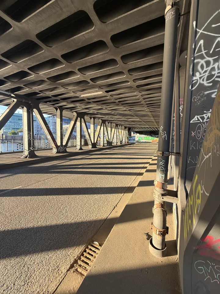 Leere Fahrbahn unter einer Stahlbrücke mit Fallrohr und Graffiti rechts, Stützenreihe links