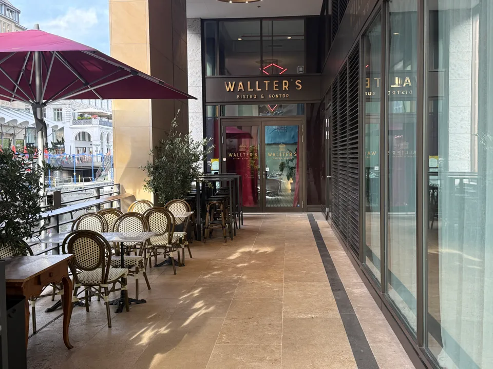 Leere Außenterrasse mit Bistrostühlen und Olivenbäumen vor dem verglasten Eingang von Wallter's Bistro & Kontor am Fleet