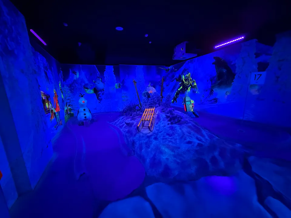 Schwarzlicht-Minigolfraum im Winterdesign mit Schneehügel, Holzschlitten, Schneemann-Figur und Roboter-Figur