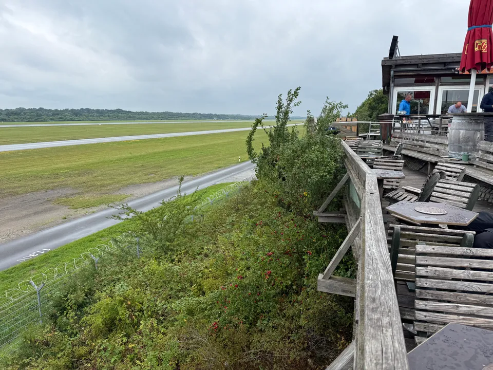 Holzterrasse am Hang über eingezäuntem Flughafengelände mit Rollbahn und Grasflächen