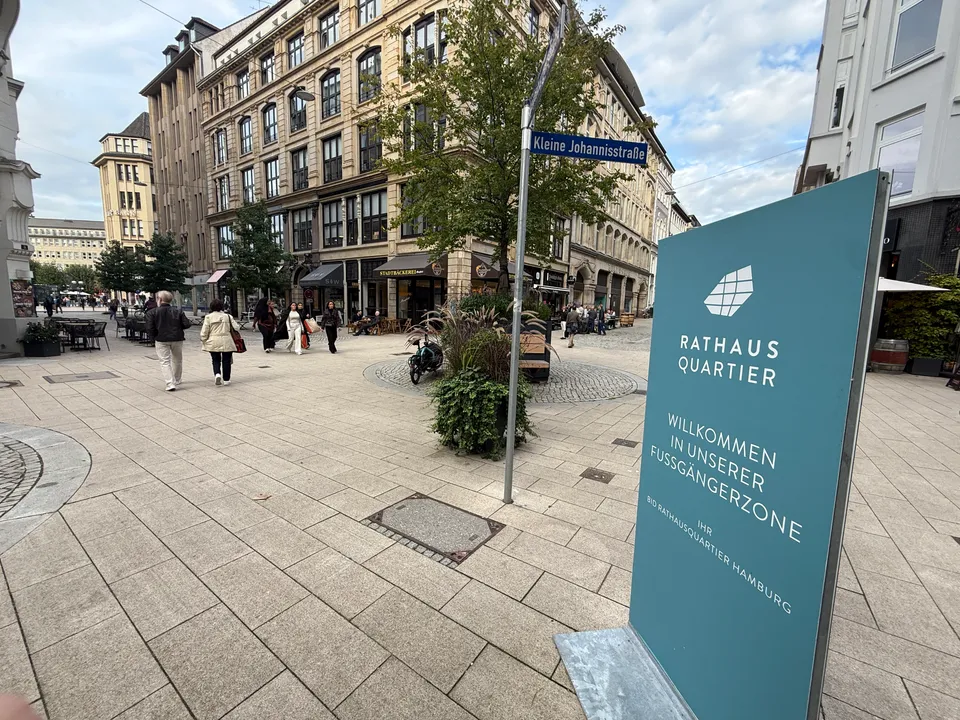 Fußgängerzone Kleine Johannisstraße mit petrolfarbener Rathausquartier-Stele, Straßenschild, Baum und historischen Geschäftshäusern