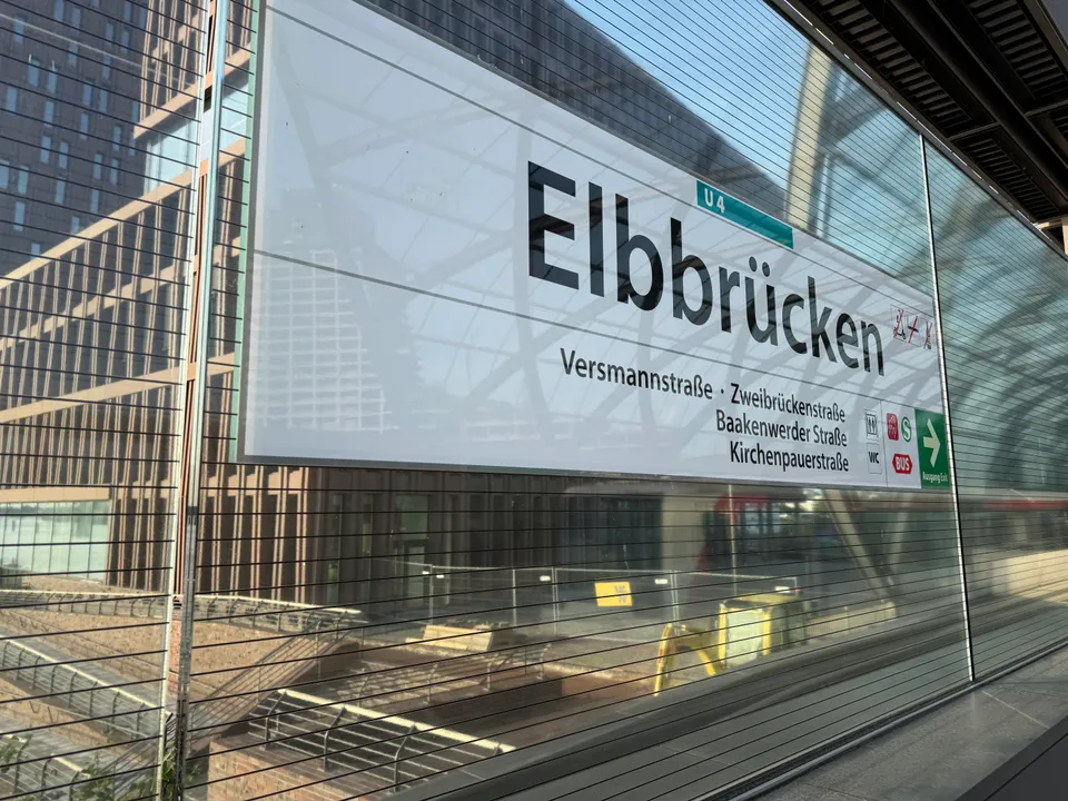 Stationsschild „Elbbrücken“ der Linie U4 hinter Glas, mit Straßennamen, Umstiegssymbolen und grünem Ausgangspfeil