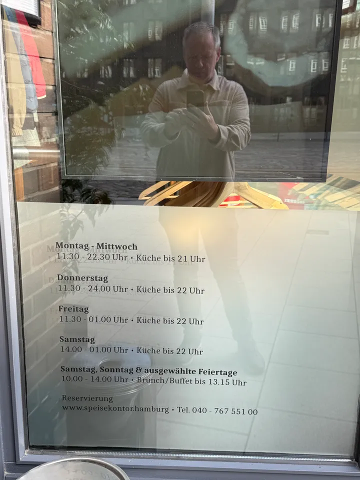 Schaufensterscheibe mit Öffnungszeiten und Reservierungshinweisen des Speisekontors, darin spiegelt sich eine fotografierende Person
