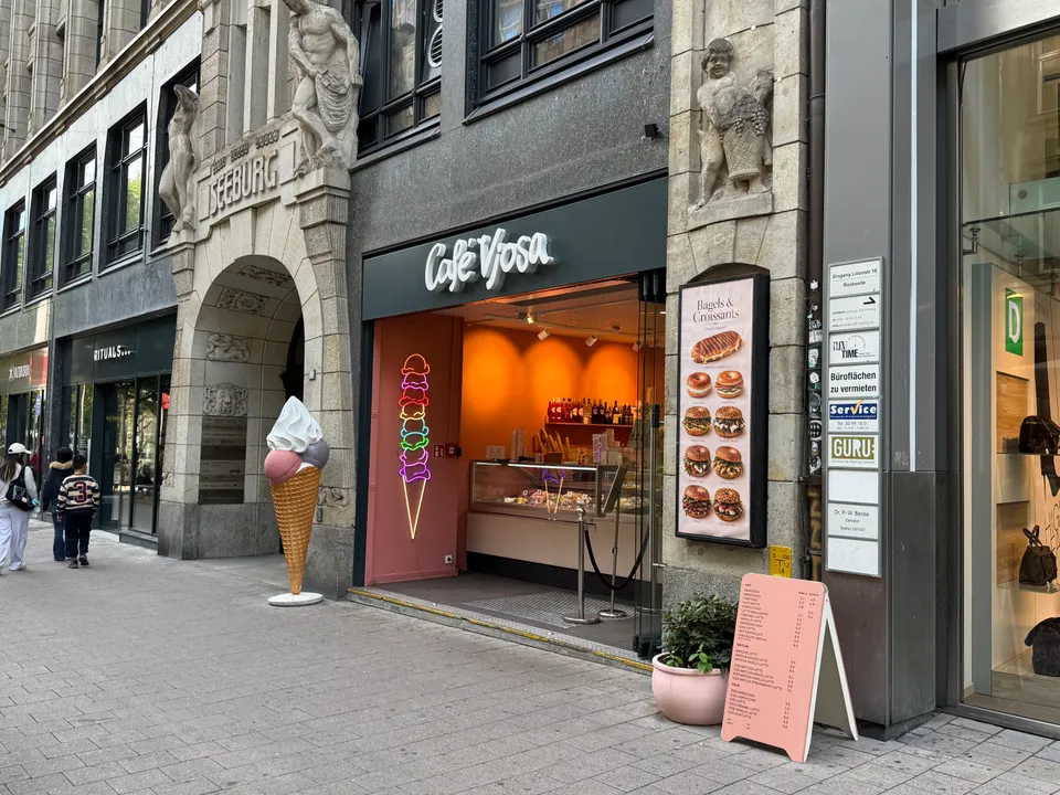 Eingang des Café Vjosa mit Leuchtschrift, Neon-Eistüte, Bagel-Plakat und großer Eistüten-Figur vor Sandsteinportal