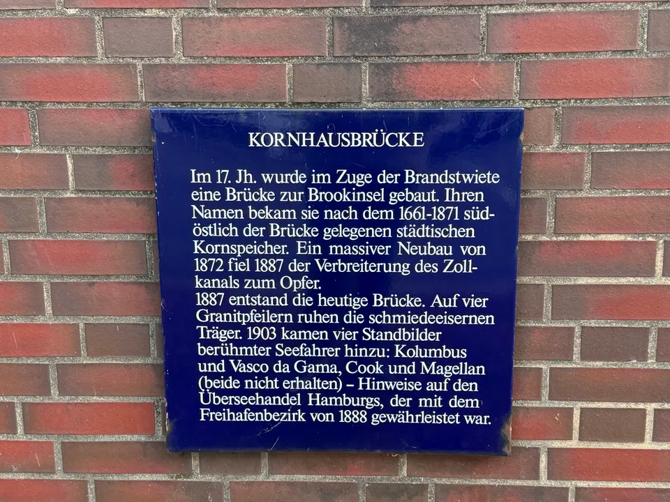 Blaue Informationstafel zur Geschichte der Kornhausbrücke mit weißer Schrift an roter Klinkerwand