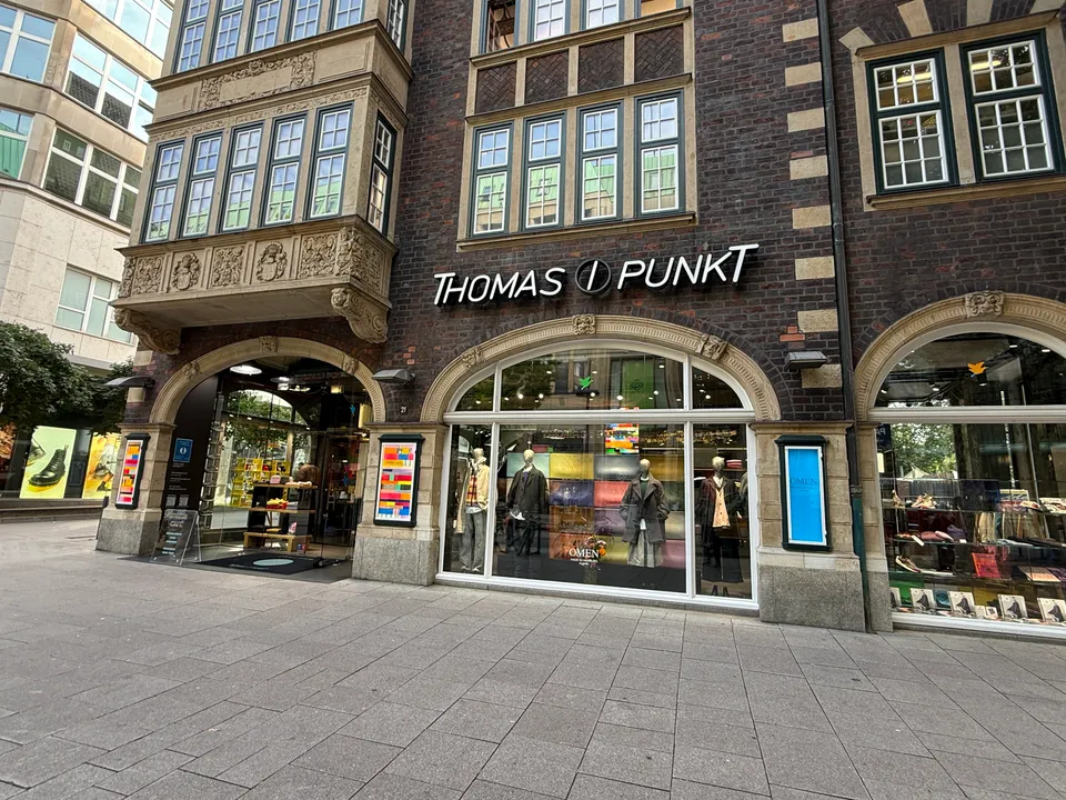 Backsteinfassade mit Sandsteinerker und Schriftzug Thomas I Punkt über rundbogigen Schaufenstern mit Schaufensterpuppen