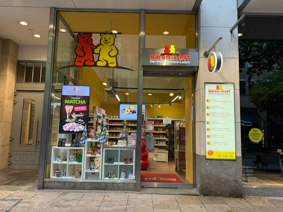 Ladenfront des Fruchtgummi-Geschäfts Bären-Treff mit Gummibären-Logo, offener Tür und gelbem Verkaufsraum mit Regalen