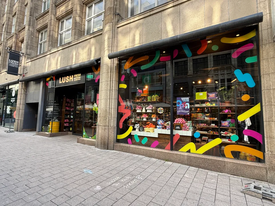 Schaufenster und Eingang des LUSH-Kosmetikladens mit bunten Fensteraufklebern an einer Natursteinfassade in der Fußgängerzone