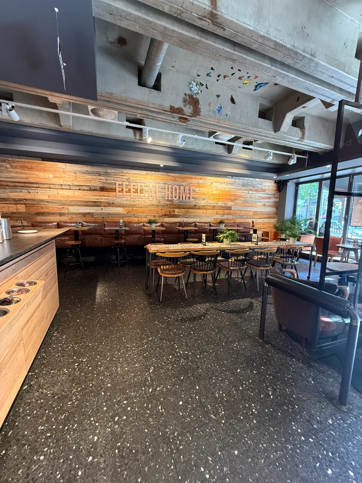 Leerer Gastraum mit Altholzwand und Schriftzug Feel at Home, Lederbank, langem Holztisch und Betondecke