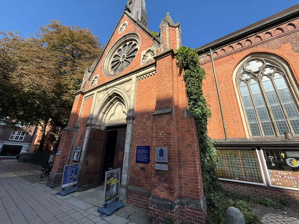 Backsteinportal einer Kirche mit Rosettenfenster, offener Holztür und Konzertaufstellern auf dem Gehweg davor