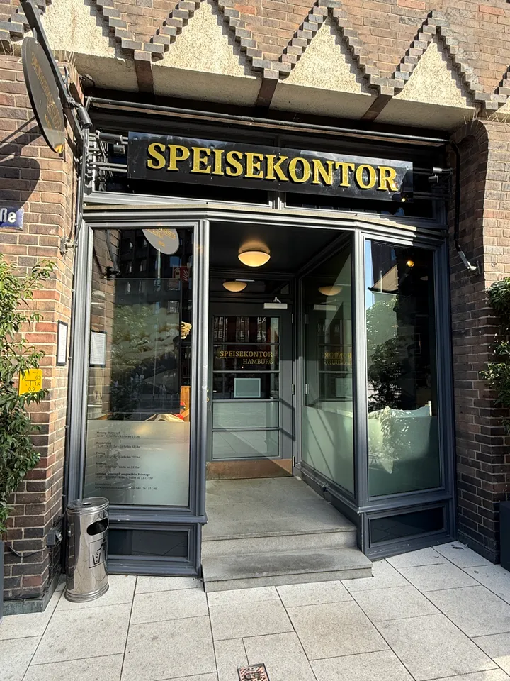 Verglaster Eingang des Speisekontors mit goldenem Schriftzug über der Tür in einer Klinkerfassade